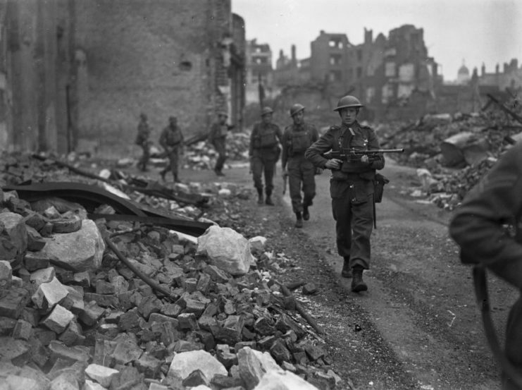Soldiers with the 48th Highlanders of Canada walking along a rubble-strewn road