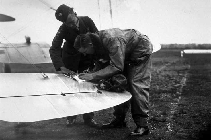 S.L Pope using the wing of his aircraft as a writing surface while a fellow serviceman watches