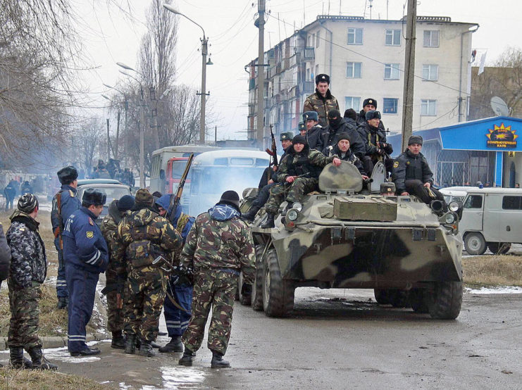 Chechen fighters sitting on top of an armored vehicle that's driving along a road