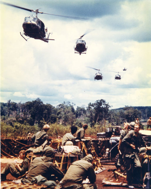 Five helicopters flying over a group of American soldiers