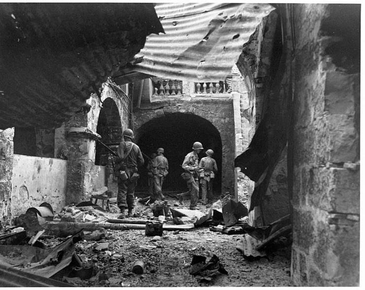 Four US infantrymen walking through a damaged building