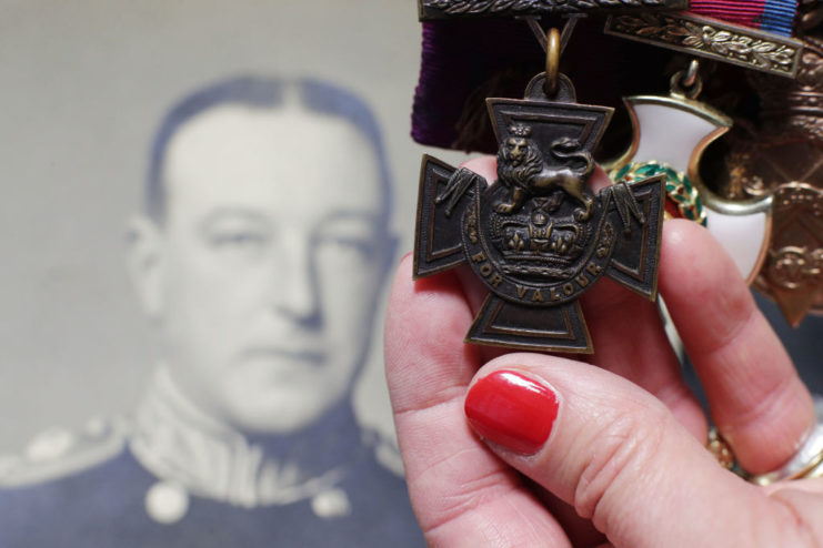 Hand holding up the Victoria Cross in front of a photo of Gordon Campbell