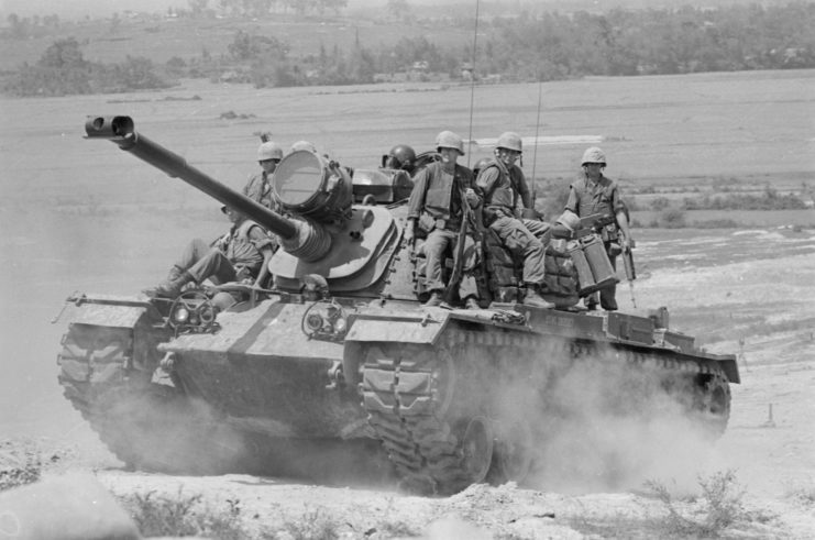 US Marines riding atop an M48A3 Patton while it's driving along a dirt road