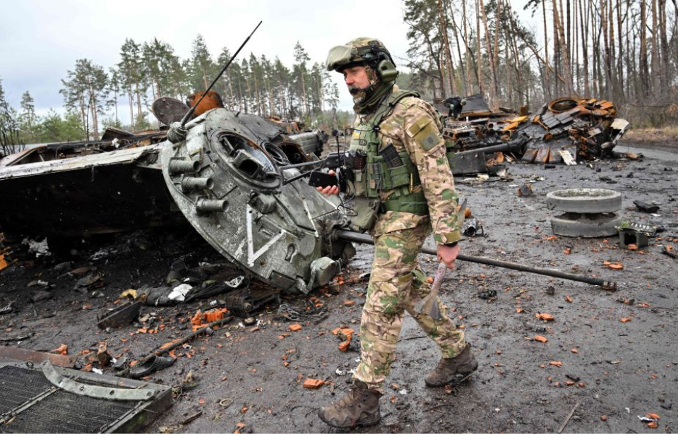 Ukrainian soldier walking by a damaged Russian tank