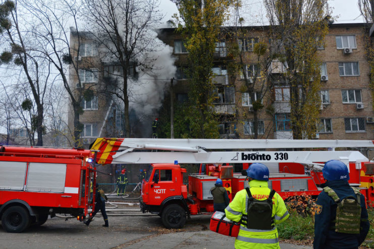 Firefighters standing outside an apartment building shrouded in smoke