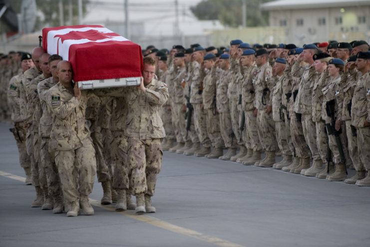 Canadian Honour Guard carrying a flag-draped casket while other soldiers stand nearby