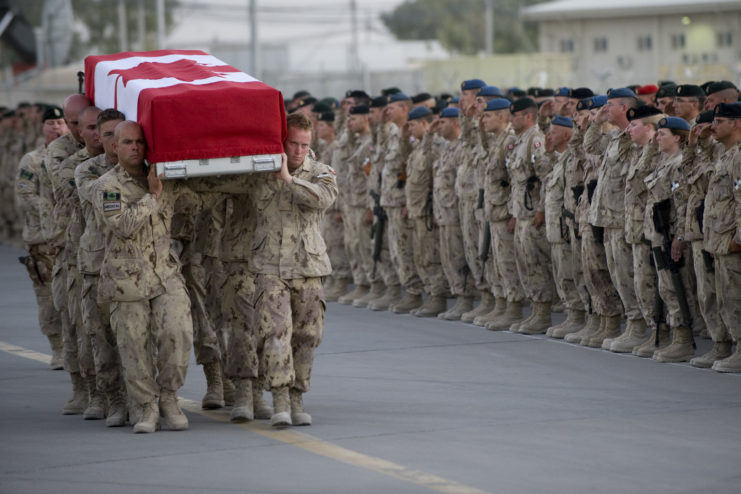 Canadian Honour Guard carrying a flag-draped casket while other soldiers stand nearby