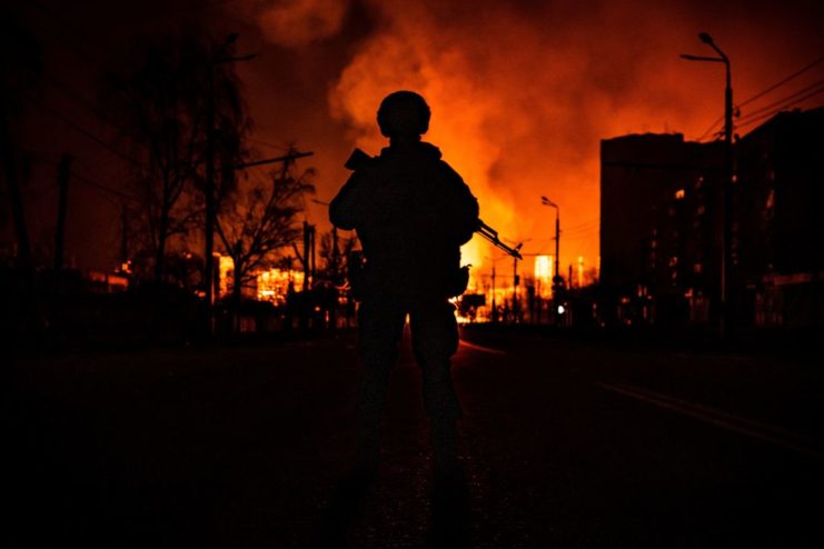Ukrainian Special Forces member standing in front of flaming buildings