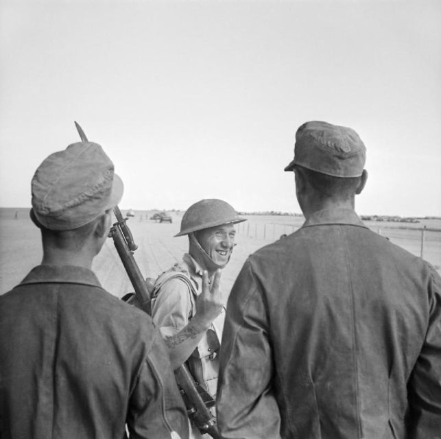 Британский солдат держит знак победы «V» на двух немецких военнопленных (военнопленных)