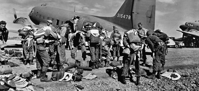 Members of the 511th Parachute Infantry Regiment, 11th Airborne Division putting on parachutes by a Douglas C-47 Skytrain