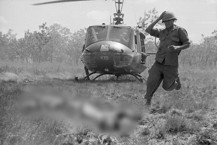 Soldier running through the grass while a helicopter is parked in the distance