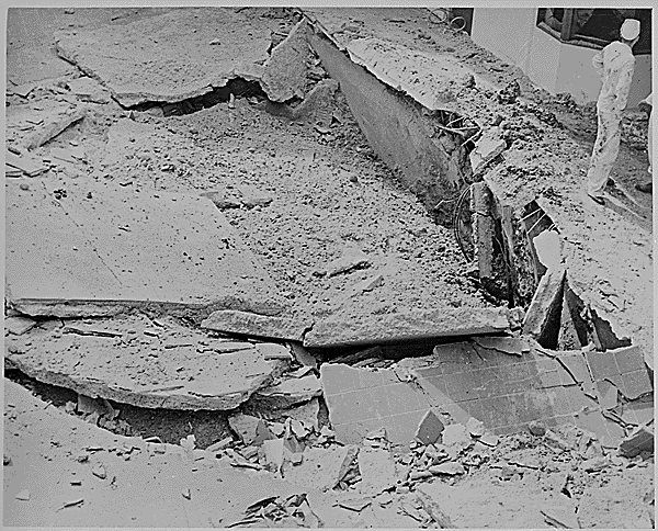 US Navy personnel standing next to a large bomb crater in the ground