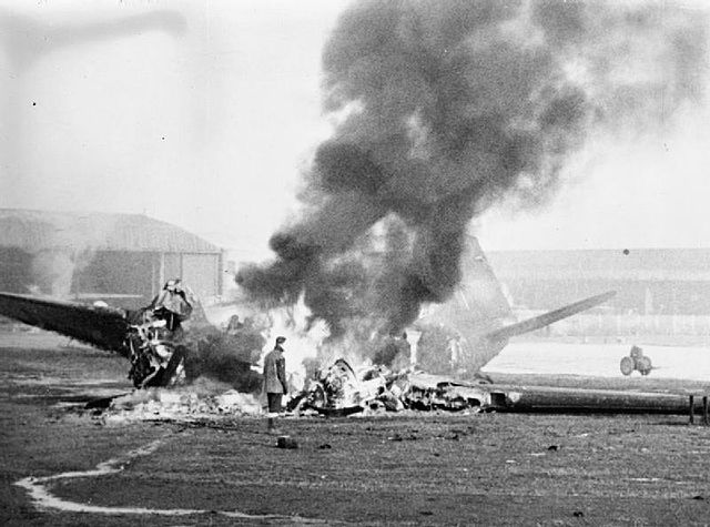 Royal Air Force (RAF) personnel standing beside a Douglas DC-3 shrouded in flames