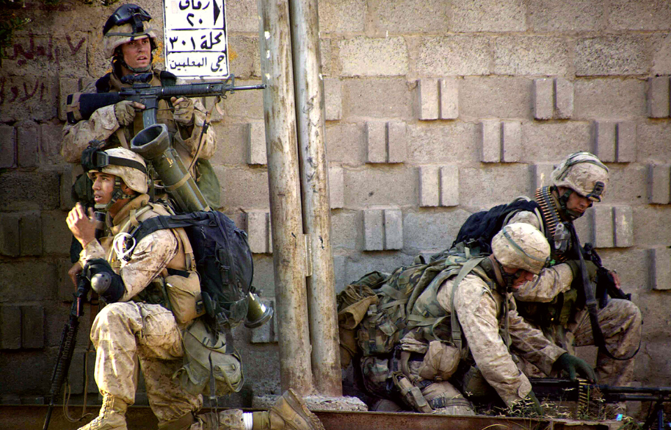 Four US Marines positioned along a stone wall
