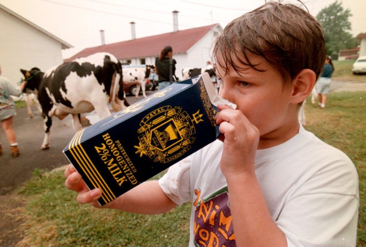 Male child drinking from a carton of milk with the US Naval Academy's logo on the exterior