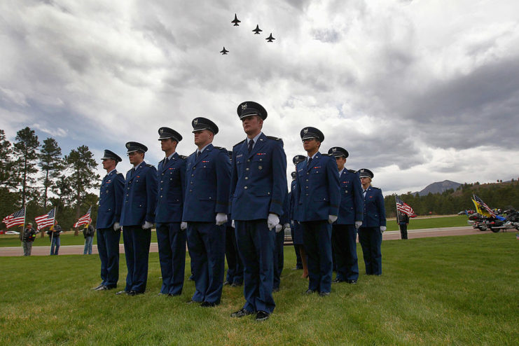 Airmen standing at attention while four General Dynamics F-16 Fighting Falcons flying overhead