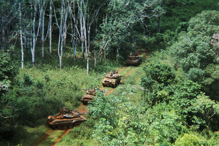 Tanks and armored personnel carriers driving through the Vietnamese jungle