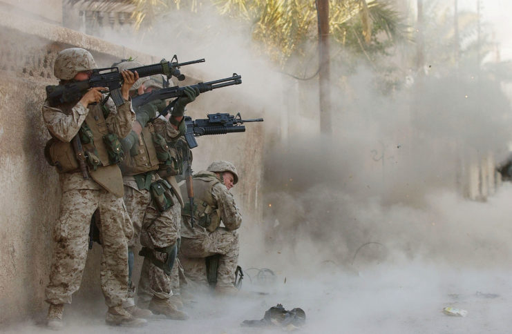 Four US Marines standing against a wall while a grenade explodes