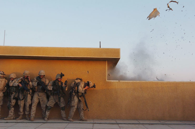 US Marines standing against a wall while a grenade explodes