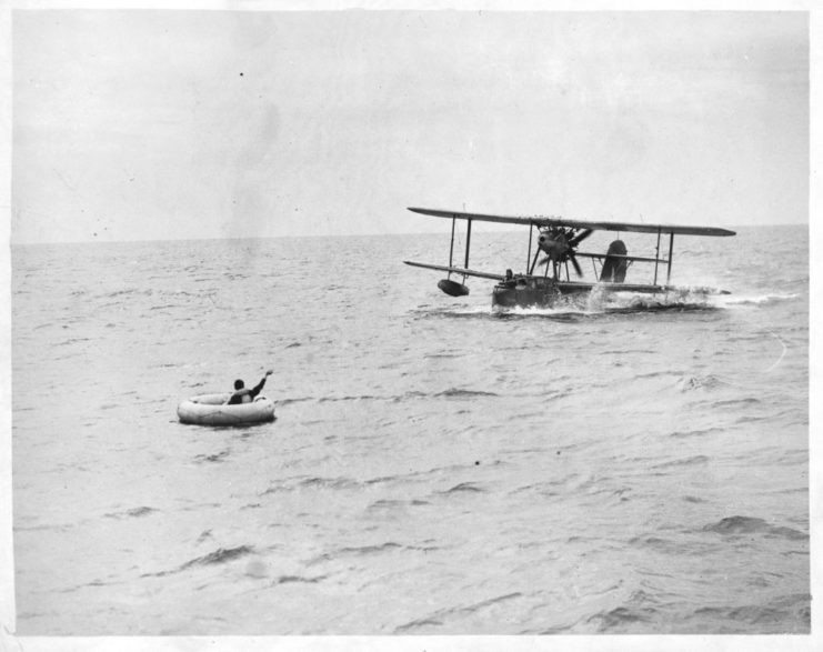 British pilot waving at a descending Supermarine Walrus as it comes in to land on the water