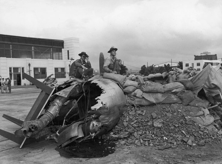 Two US Navy personnel sitting on the remains of a damaged aircraft at Hickam Field