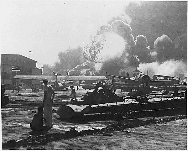 US Navy personnel looking at flames and smoke rising into the sky in the distance