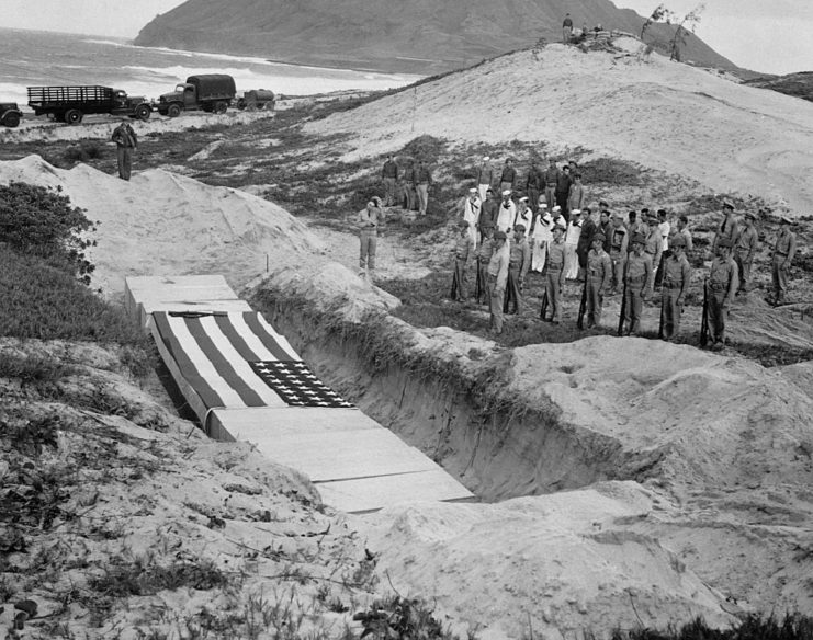 US military personnel standing along a mass grave for those killed during the attack on Pearl Harbor