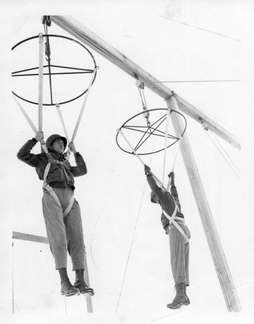 Two doctors with the First Special Service Force (1SSF) hanging from practice parachute harnesses