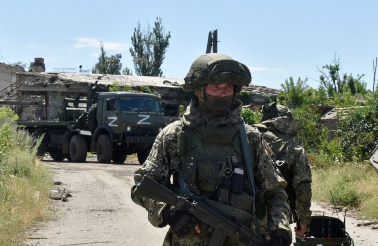 Russian soldiers standing near a military vehicle parked along a dirt road