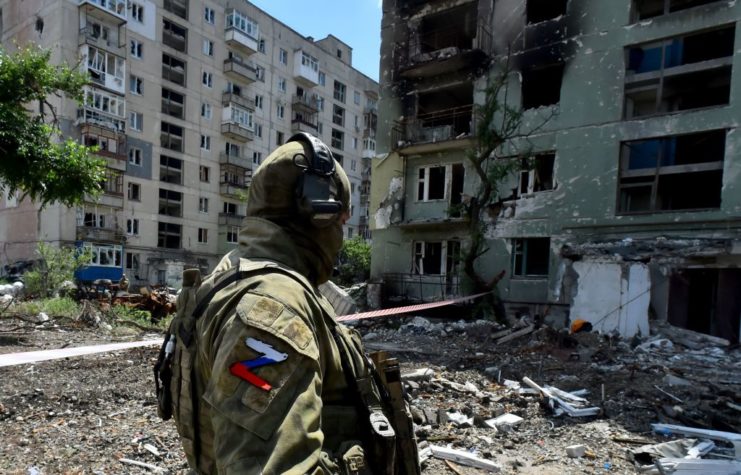 Russian soldier standing near a severely-damaged apartment building