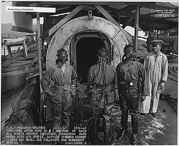 Four US Navy personnel standing on the wreck of the USS Oklahoma (BB-37)