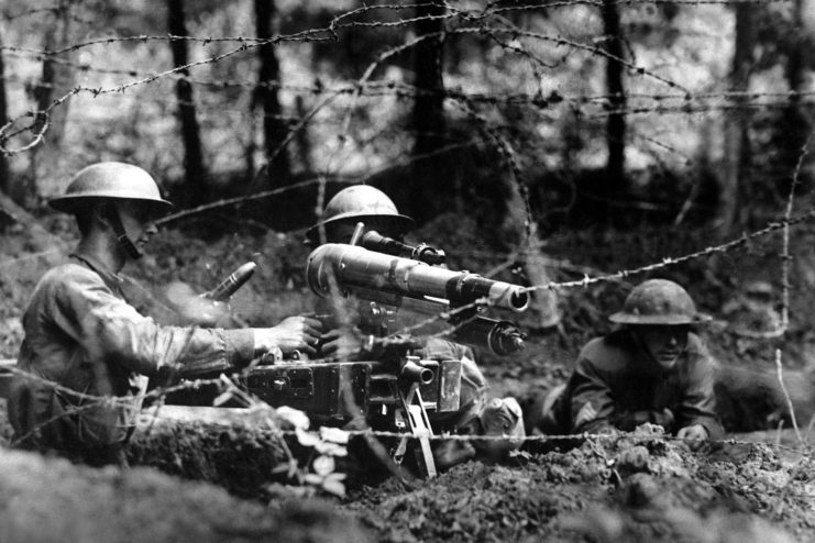 Three soldiers manning a 37 mm M1916 from behind rows of barbed wire