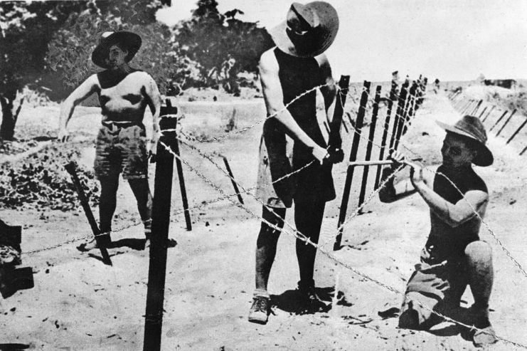 Three Australian soldiers setting up a barbed wire fence