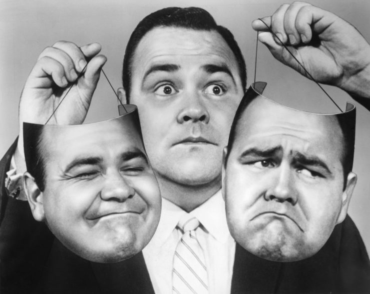 Jonathan Winters holding two masks of his own face