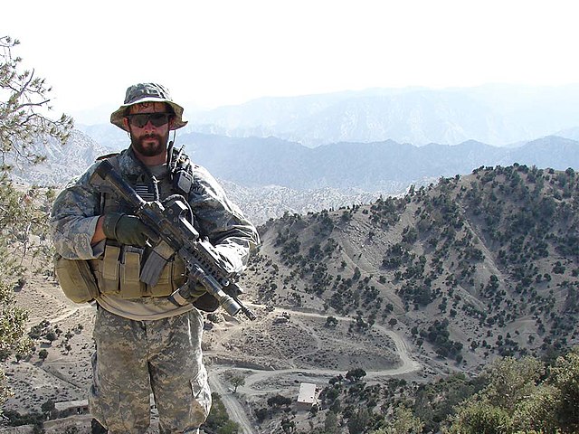 Staff Sgt. Ronald J Shurer II standing with his rifle in the middle on the Afghan desert