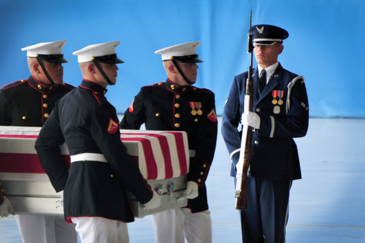 US Air Force Honor Guard ceremonial guardsmen carrying an American flag-draped coffin with another presents arms