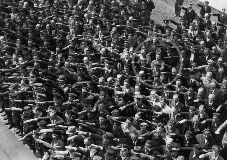 Blohm+Voss employees performing the German salute, while August Landmesser stands with his arms crossed over his chest