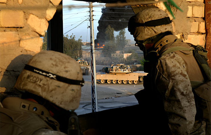 Two US Marines looking at tanks through a hole in a wall