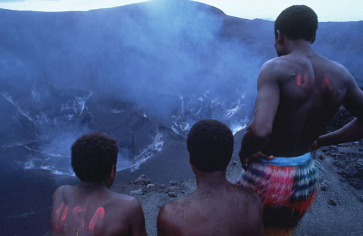 Three men looking into the center of Mount Yasur