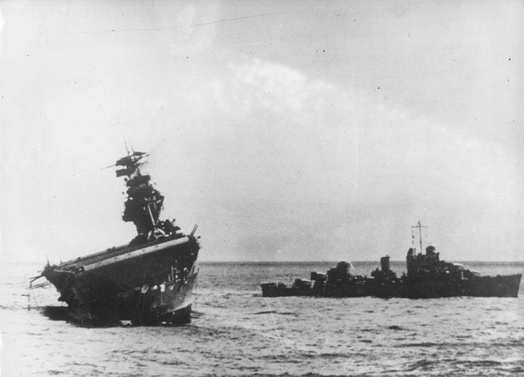 USS Yorktown (CV-5) listing to one side in the water while another ship sails nearby