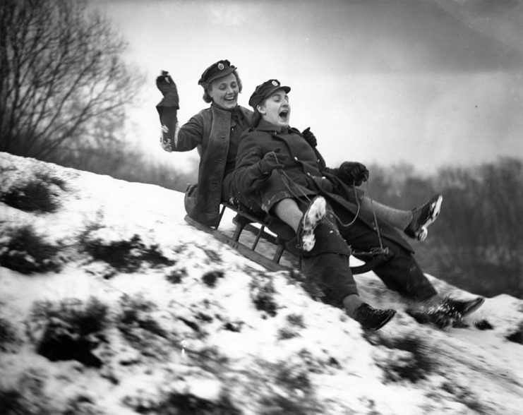 Two women with the Auxiliary Territorial Service (ATS) riding a toboggan down a snowy hill