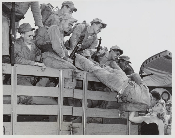 Soldier leaning out of the bed of a truck to kiss his girlfriend while his comrades watch