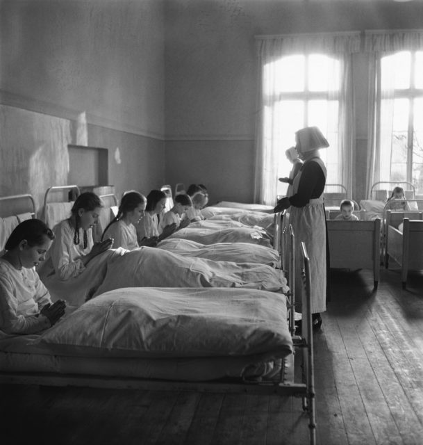 Red Cross and Protestant relief workers standing before female children praying in their beds