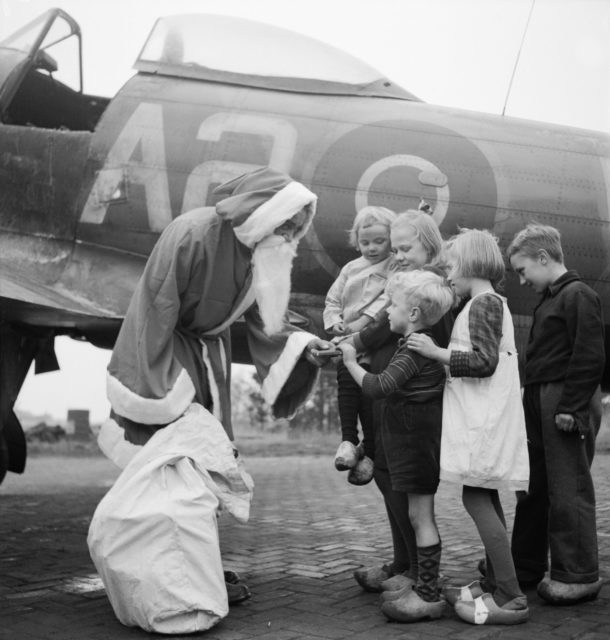 Leading Aircraftman Fred Fazan dressed as Santa Claus, handing out presents to children