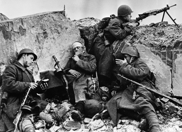 Three Red Army soldiers resting behind a trench while a fourth stands guard