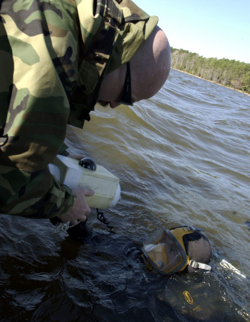 Boatswain's Mate 2nd Class Arick Hiles handing a compact sonar unit to Damage Controlman First Class Ralph Leete