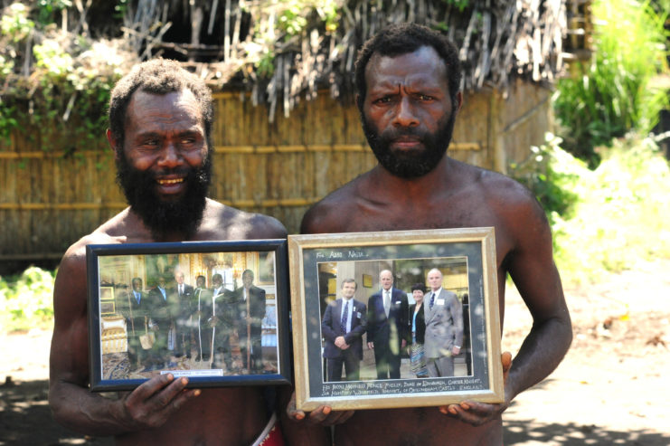 Two Yaohnanen tribesmen holding framed photos of Prince Philip