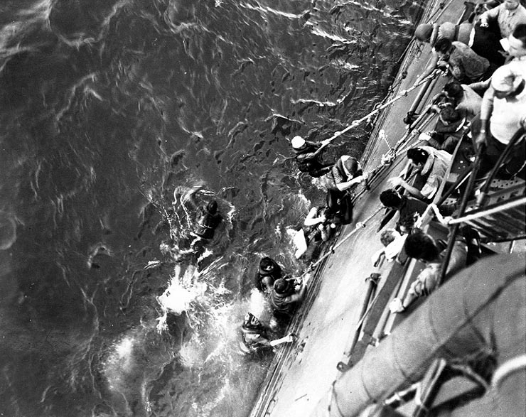 Crewmen aboard a ship pulling survivors from the ocean