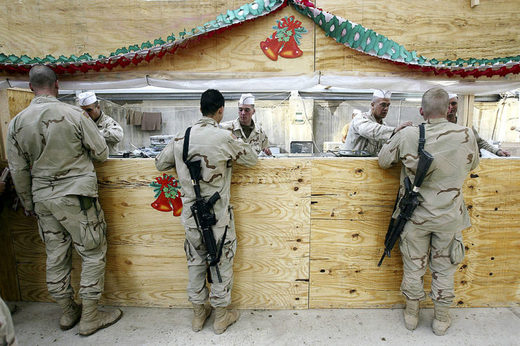 US military cooks presenting Christmas dinner to three members of the US Army's 4th Infantry Division