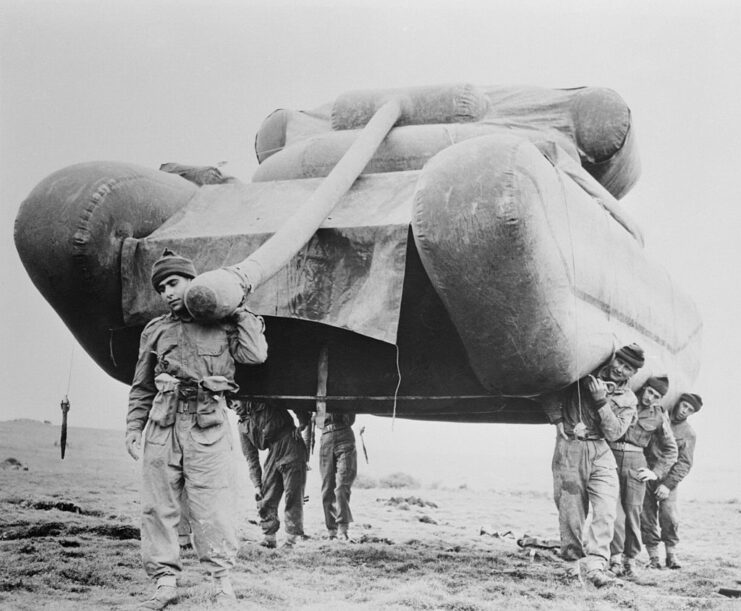 Six British soldiers carrying an inflatable tank across a beach